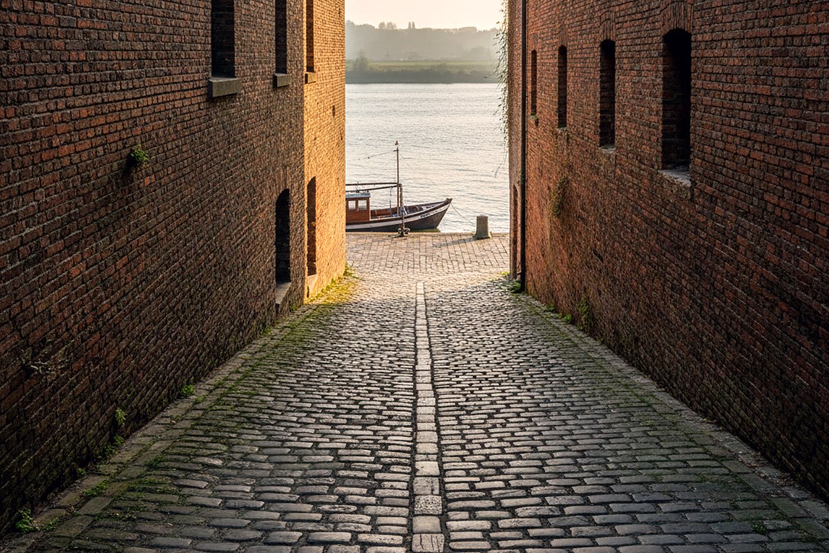 A steep cobbled ramp of worn stone leading down between old brick warehouse walls
