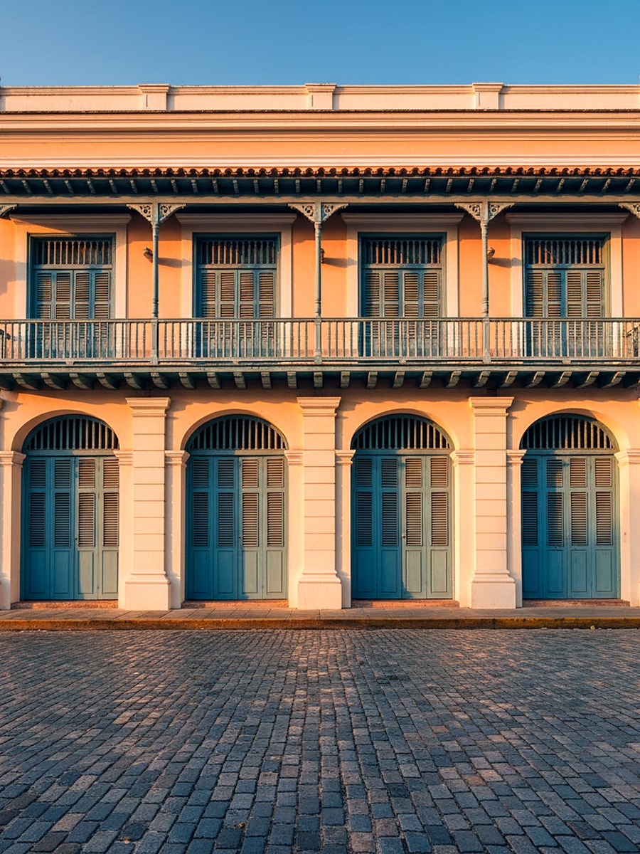 A tall pastel facade with wooden balconies above a blue cobbled street in warm evening light